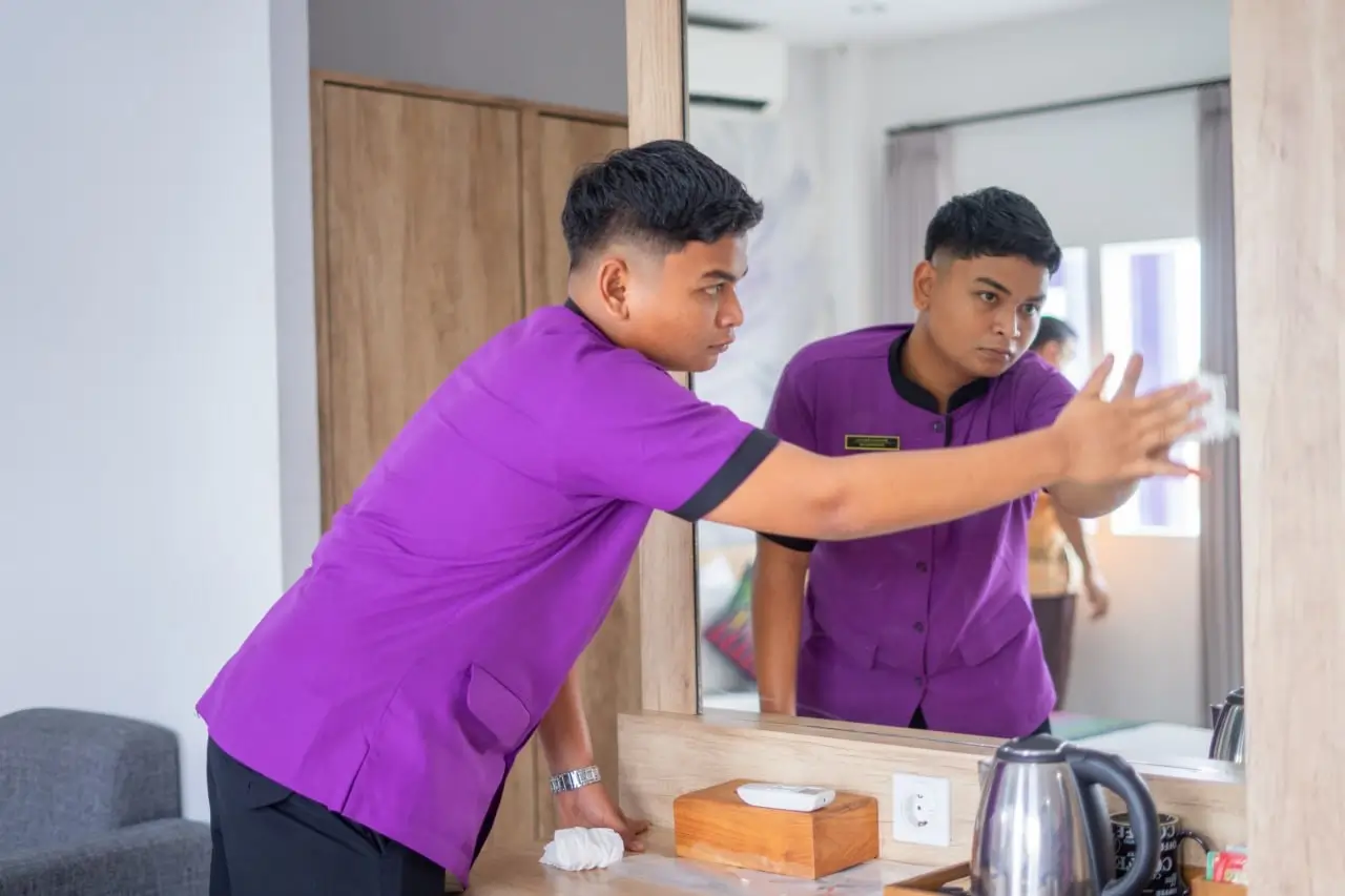 HIS Student melakukan praktik housekeeping dengan membersihkan cermin kamar hotel